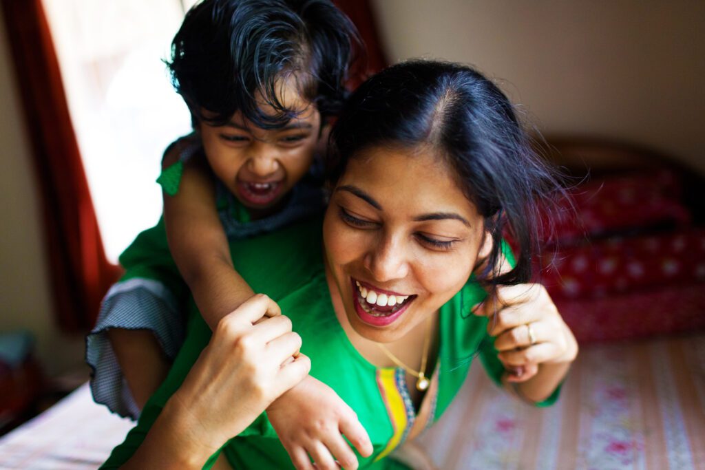 smiling South Asian woman giving her toddler a piggy-back ride shareourstrength.org